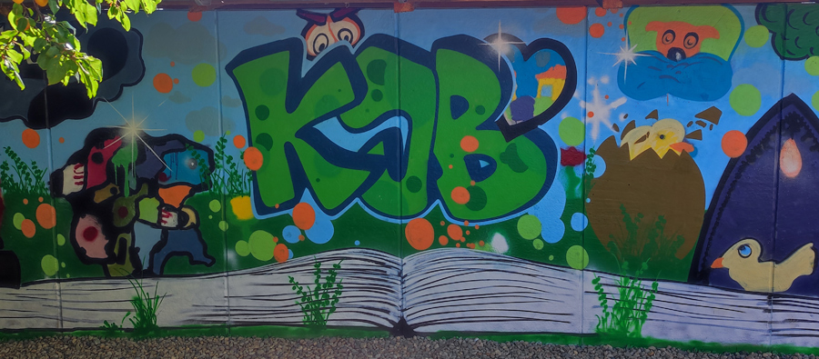 Graffiti-Workshop vom 1. bis 5. August 2022 auf dem KJB Nickern. | Ein buntes Graffiti zeigt ein aufgeschlagenes Buch, darüber die Buchstaben KJB mit einem Herz. Über dem K lugt eine Eule hervor.