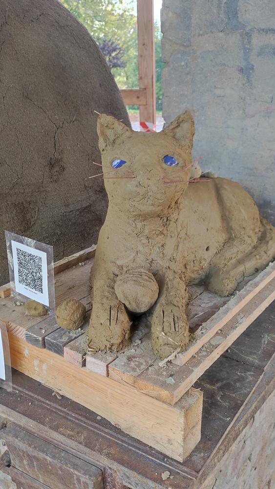 Liegende Katze mit erhobenem Kopf aus Lehm mit blauen Augen.